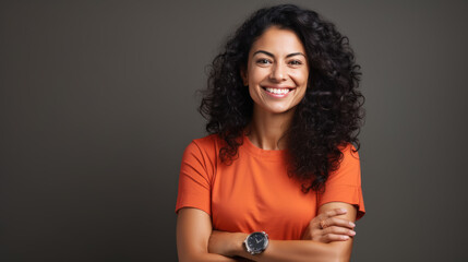 Wall Mural - Confident woman with curly hair, smiling at the camera, wearing a bright orange shirt, with her arms crossed.