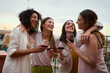 © CarlosBarquero - Happy group of millennial women holding glasses red wine gathered embracing celebrating summer party rooftop. Joyful young adult female friends hugging having fun together enjoying vacation outdoors