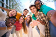 © CarlosBarquero - A large multiracial group of teenagers taking a selfie looking front camera laughing and having fun piggybacking together outdoor. Young students enjoying their free time with friends in street city