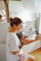 Poster - Beautiful woman taking care of skin by applying moisturizer cream in bathroom