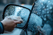 close up of a hand wiping a wet car rearview mirror with a rag