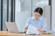 © SOMKID - Asian accounting woman working with document paper and laptop computer at table office, Financial and accounting woman concept.