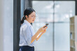 © SOMKID - Asian businesswoman using smartphone standing at the office.