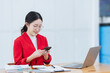 © SOMKID - Asian businesswoman wearing a suit using smartphone with digital laptop computer working at modern office, Asian beautiful businesswoman in red suit working in the modern office.