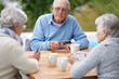 © AW/peopleimages.com - Poker, playing cards and senior group in retirement, outdoor and relaxed in garden, backyard and terrace. Elderly people, bridge and smile with coffee, table and outside for relaxation, fun and games