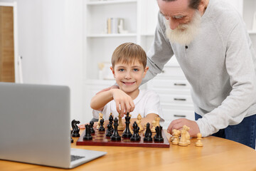 Poster - Grandfather teaching his grandson to play chess following online lesson at home