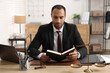 © New Africa - Serious lawyer reading book at table in office