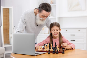 Wall Mural - Grandfather teaching his granddaughter to play chess following online lesson at home