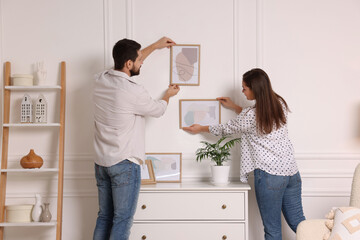 Canvas Print - Man and woman hanging picture frames on white wall at home