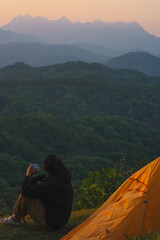 Wall Mural - nature traveling with orange camping tent and layer of mountain with solo man drink coffee and see sunrise