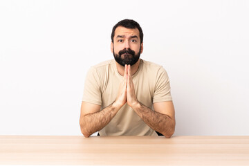 Wall Mural - Caucasian man with beard in a table keeps palm together. Person asks for something.