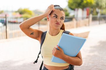 Wall Mural - Young pretty student woman at outdoors having doubts and with confuse face expression