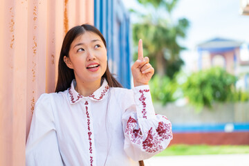 Wall Mural - Young Chinese woman at outdoors intending to realizes the solution while lifting a finger up