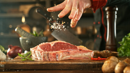 Wall Mural - Close-up of falling salt on tasty beef steak in kitchen. Chef in background.