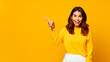 © Ivan Guia - Young excited beautiful happy brunette woman pointing away and smiling isolated on yellow background. Copy space design