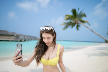 Wall Mural - Woman in yellow bikini taking selfie near the coconut palm trees on tropical beach.