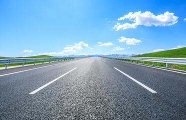 Straight asphalt road and green meadow with mountain nature landscape under blue sky