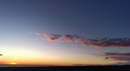 La Luna all’alba resta ancora nel cielo sopra le nuvole rosa sulla colline mentre il sole sorge dal mare