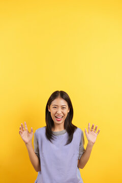 Young women making claw gesture and roaring while imagining tiger isolated on yellow background