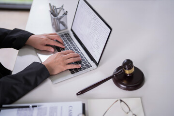 Male lawyer typing data and reading financial document of business on laptop to analysis about legal agreement and terms of business contract while working on the desk with hammer in law firm