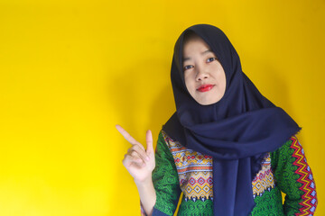 Excited beautiful Asian girl wearing hijab pointing finger to open palm, advertising something isolated on yellow background