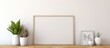 © Lasvu - An empty picture frame is placed on top of a wooden shelf. The shelf is adorned with a small plant, adding a touch of greenery to the scene.