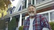 Mature man smiling, and wearing flannel shirt with a handsome beard, in front of a house.