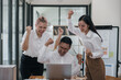 © amnaj - Three ecstatic asian business professionals celebrating a victory with a fist pump in a modern office.