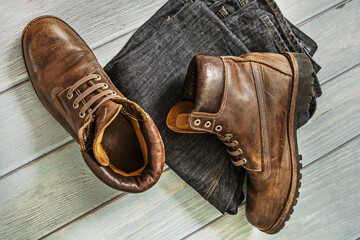 A pair of brown leather hiking boots with folded jeans on a light wooden surface