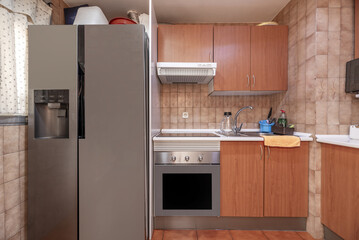 Frontal image of kitchen with brown furniture, white countertop, large refrigerator, matching oven and brown stoneware floor