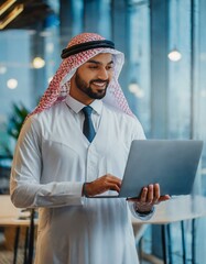 Successful muslim businessman in traditional white Kandura uses laptop in his modern office