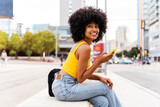 Fototapeta Nowy Jork - Beautiful young black woman with curly afrp hair style and colorful clothing strolling  outdoors in the city