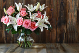 Fototapeta Kwiaty - A composition of pink roses and white lilies, arranged in a glass vase on a wooden table