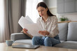 © Prostock-studio - Worried young woman reviewing documents at home