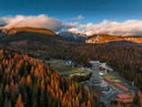 Fototapeta Londyn - Strbske Pleso, Slovakia - Aerial view of the Strbske Lake area with autumn foliage, sightseeing tower and the High Tatras mountains at background on an autumn afternoon at sunset with warm sunlight
