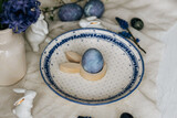 Fototapeta Tulipany - Happy Easter! Stylish easter egg in bunny figurine on vintage plate and spring flowers on linen, rustic table setting. Natural painted blue eggs and hyacinth blooms. Modern minimal still life