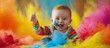A joyful baby gives a thumbs up amidst a burst of colorful powder