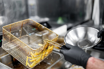 Wall Mural - Freshly fried golden French fries being transferred from a metal basket to a stainless steel bowl in a commercial kitchen.