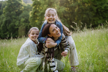 Wall Mural - Beautiful mother with two daughters, embracing at meadow. Concept of Mother's Day, maternal love.