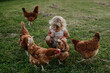 Little girl squating among chickens on a farm, chasing them. Having fun during the holidays at her grandparents' countryside home.