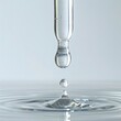A close-up of a single clear droplet of serum about to drip from the tip of a transparent dropper, with the dropper's end visible and a small pool of serum glass bottle beneath it