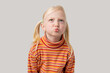 Portrait of a little girl with blond hair in a striped T-shirt blowing a kiss isolated over grey background.
