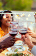 © Xavier Lorenzo - Group of young people toasting red wine at summer rooftop night party. Multiracial friends celebrating together at home terrace. Vertical photo.