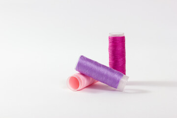 Close-up of bobbins of sewing thread in different pastel shades on a white background.