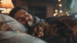 A man is laying on a bed with a cat on his lap. The cat is orange and has a fluffy tail. The man is smiling and seems to be enjoying the company of his pet. Concept of warmth and comfort