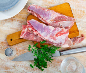 Wall Mural - Raw meaty pork ribs slabs with fresh greens ready for cooking on wooden cutting board..