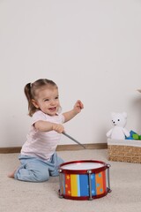 Wall Mural - Cute little girl playing with drum and drumsticks at home