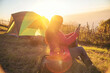 © aFotostock - Women camping outdoor sitting Tent Camp trip hiking mountain hill on sunrise. Tent camp in nature background flare sunlight mountain. Picnic green nature campground Adventure Travel wildness forest