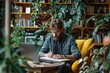 © Sariyono - Focused bearded man working on a laptop in a cozy home office surrounded by plants, concept of remote work and creative workspace