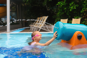 Wall Mural - Child playing in aqua park. Kid having fun and entertaining in indoor swimming pool. Toddler girl making splashes with sprinkle 